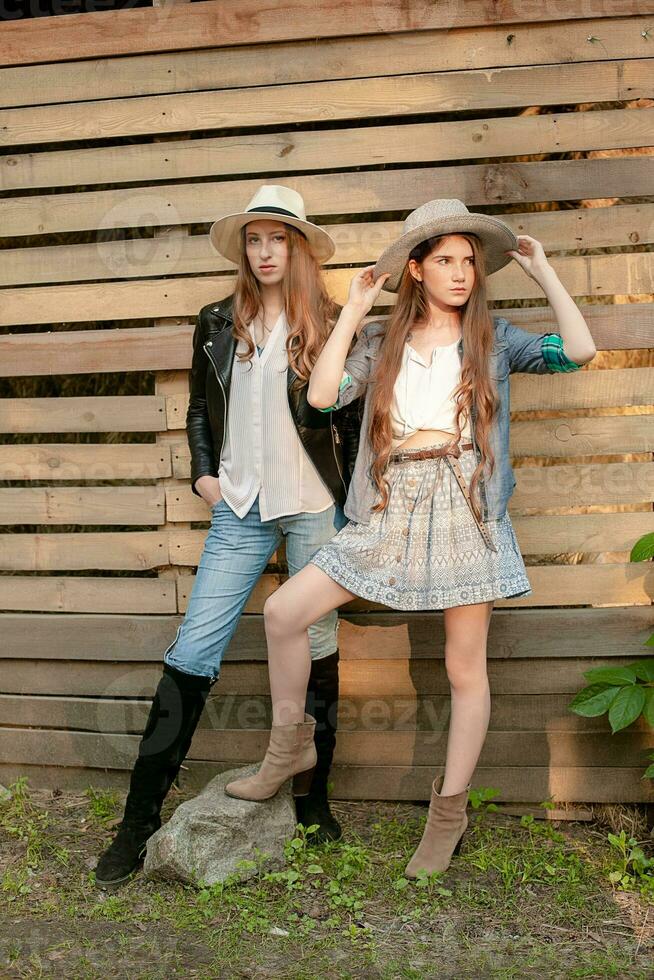 Two teenage girls wearing country style clothes standing against wooden planks wall background photo