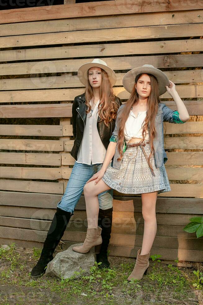 Two teen girls in rustic style clothes and wide-brimmed hats posing on wooden boards background photo