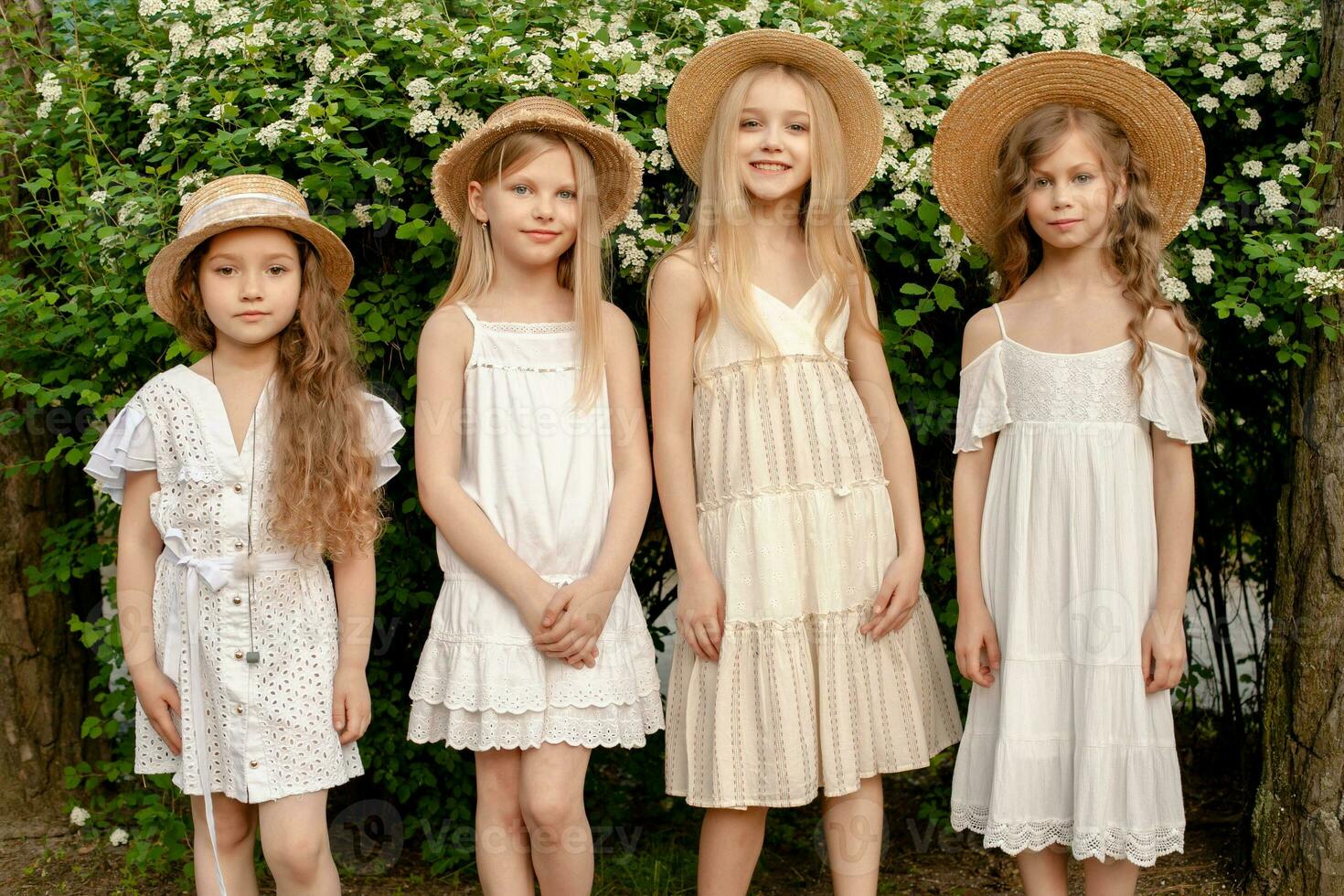 Smiling tween girls standing in summer park near green blooming bush photo