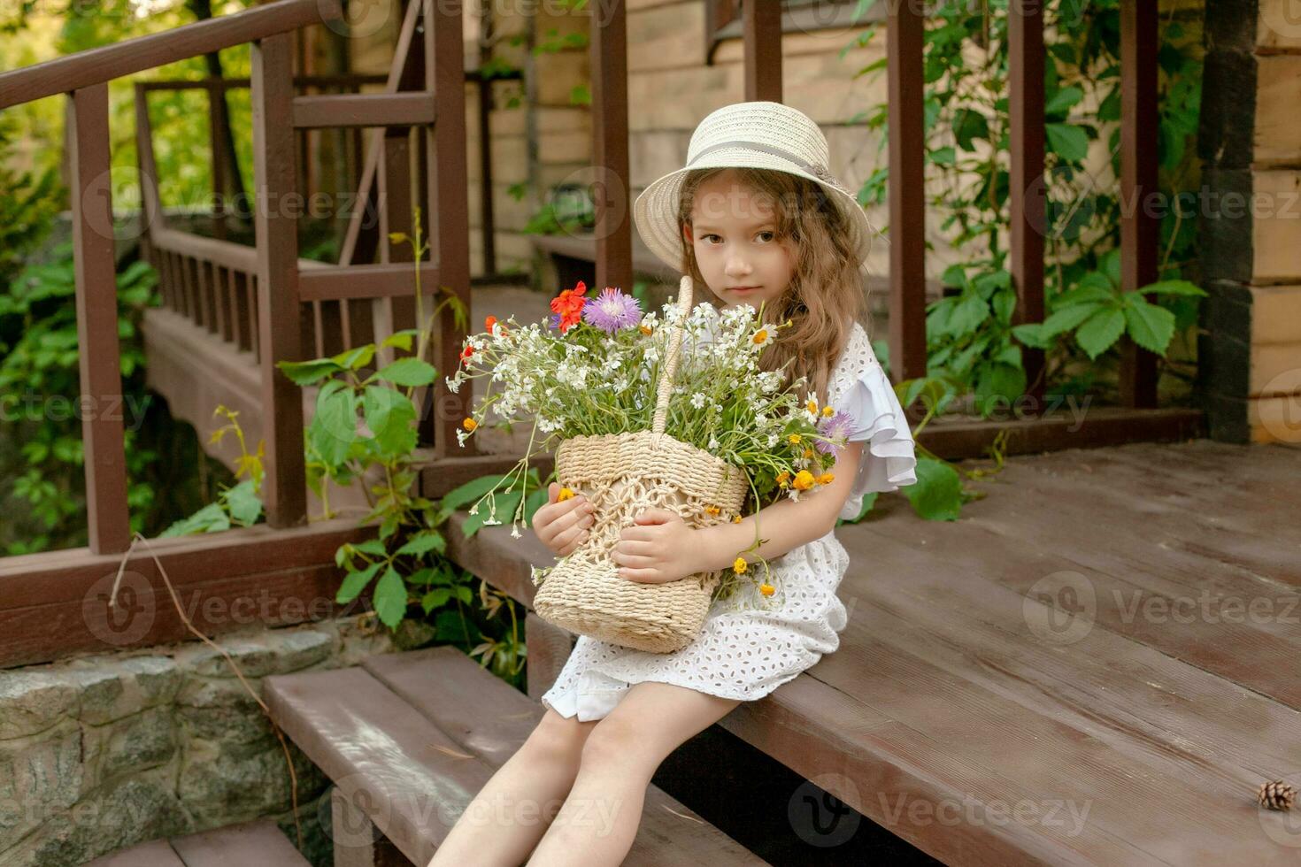 ute little girl sitting on country house threshold with basket of wildflowers photo