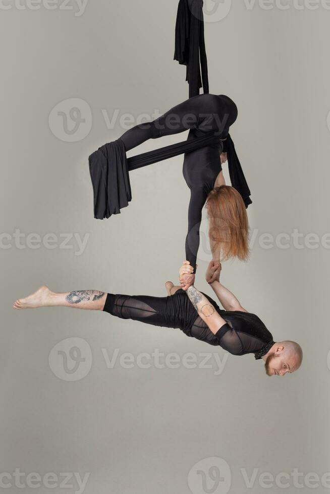 Beautiful girl and an athletic man in a black sport suits are performing an acrobatic elements in a studio. photo