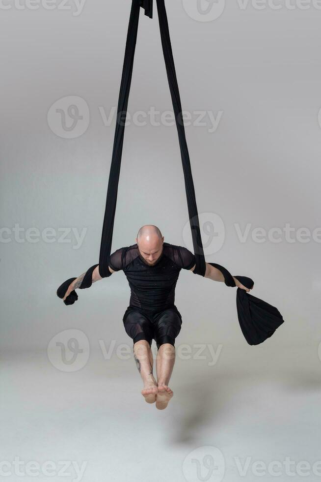 Athletic man in a black sport suit is performing an acrobatic elements in a studio. photo