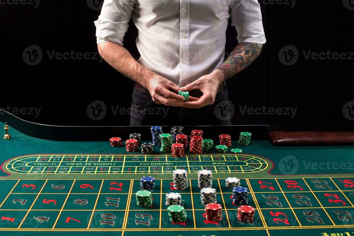 A close-up vibrant image of green casino table with roulette, with the hands of croupier and multicolored chips. photo