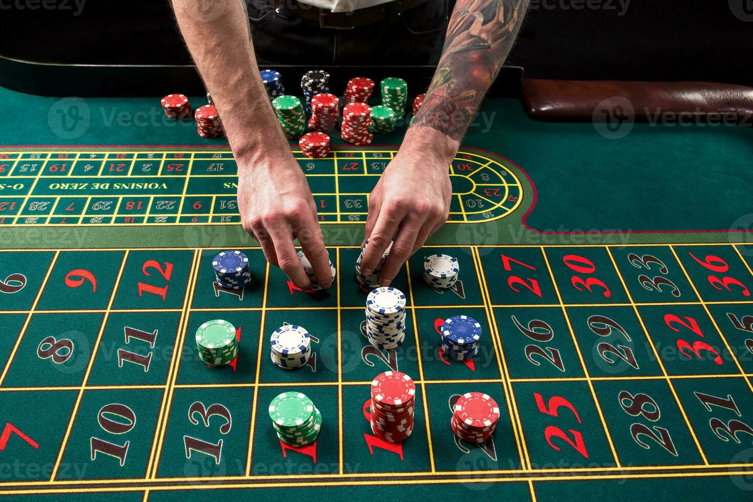 A close-up vibrant image of green casino table with roulette, with the hands of croupier and multicolored chips. photo