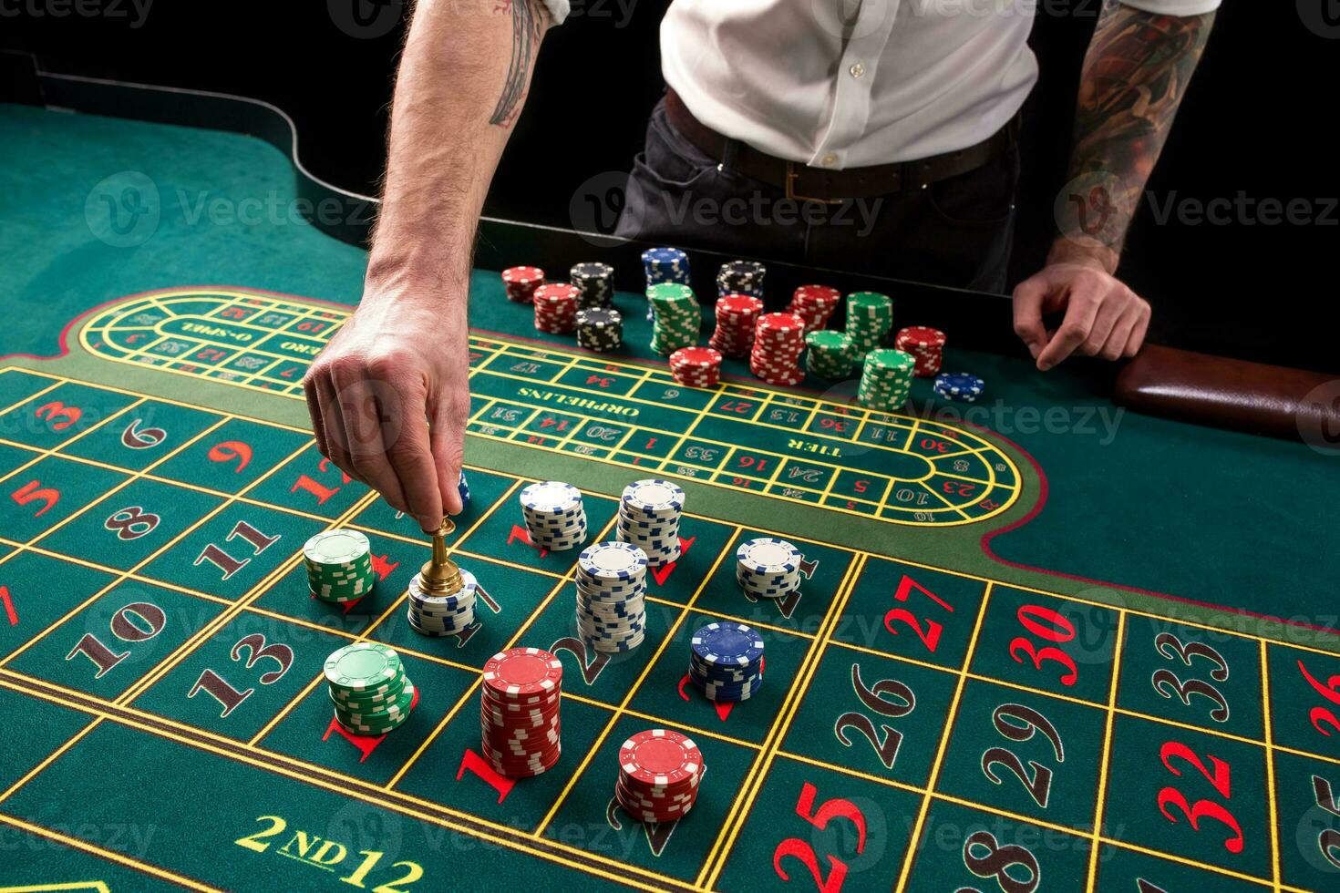 A close-up vibrant image of green casino table with roulette, with the hands of croupier and multicolored chips. photo