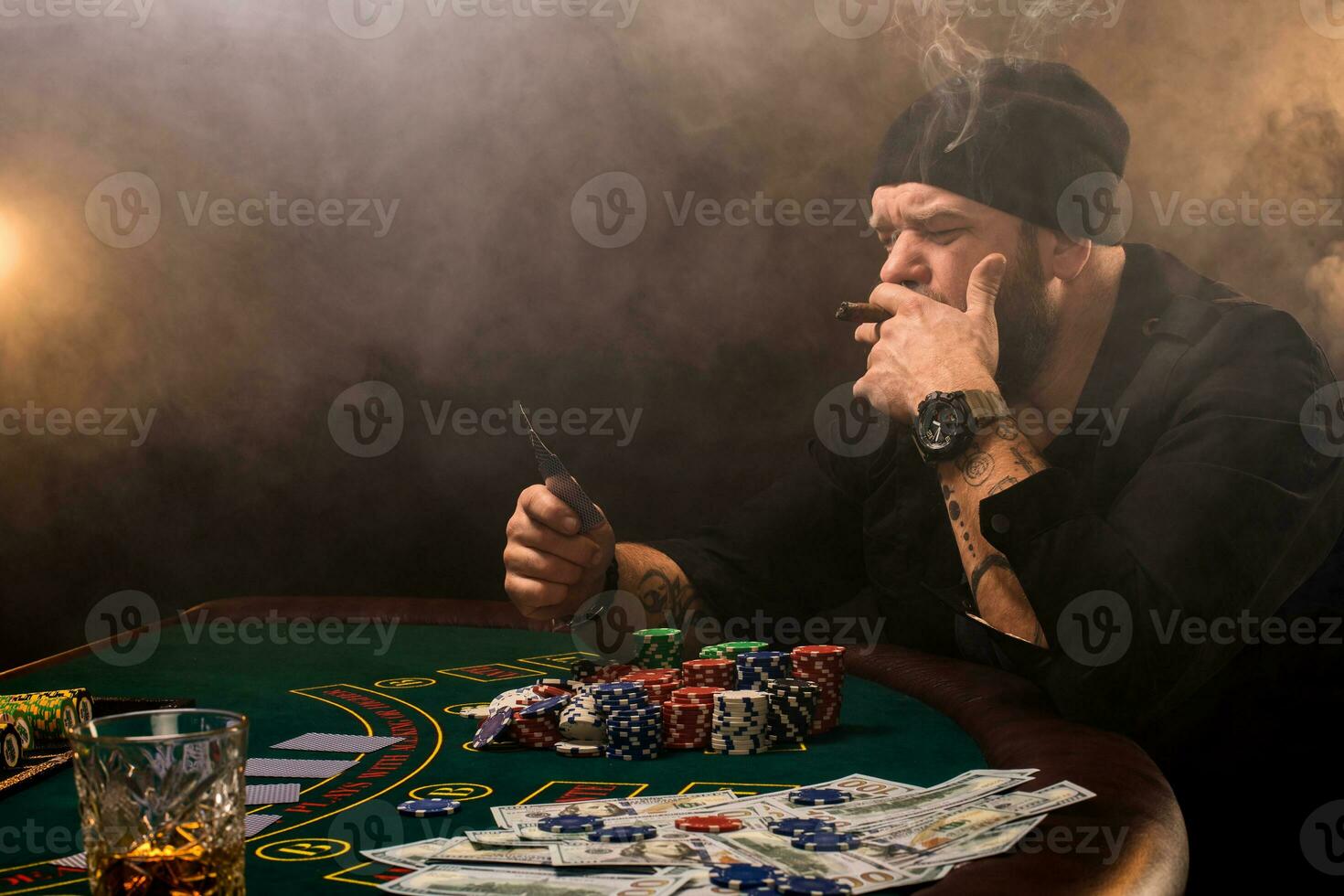 barbado hombre con cigarro y vaso sentado a póker mesa en un casino. juego, jugando tarjetas y ruleta. foto