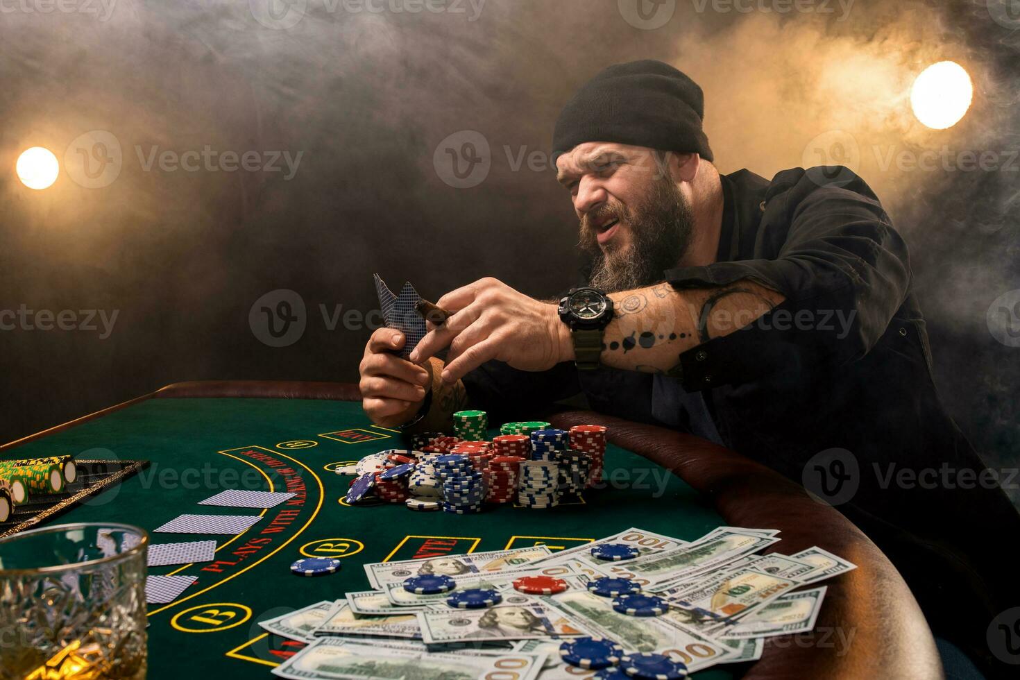 barbado hombre con cigarro y vaso sentado a póker mesa en un casino. juego, jugando tarjetas y ruleta. foto