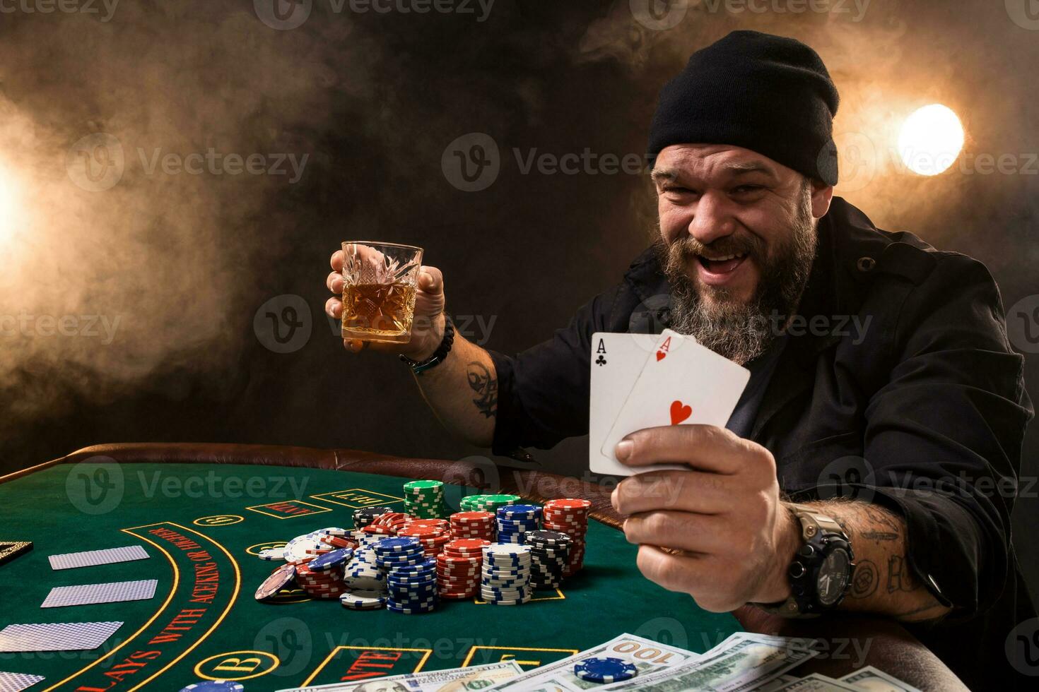 Man is playing poker with a cigar and a whiskey, a man show two cards in the hand, winning all the chips on the table with thick cigarette smoke. photo