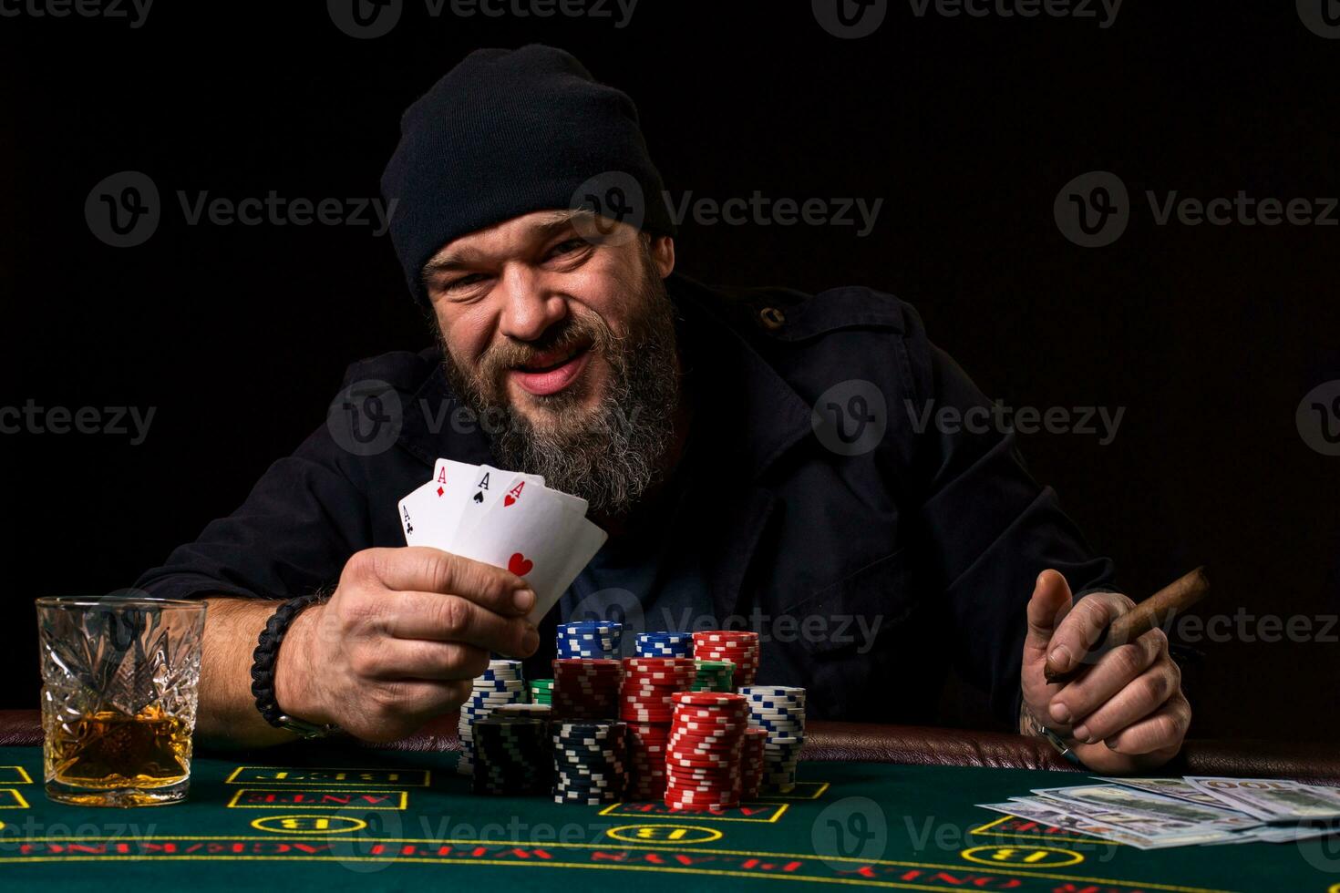 Bearded man with cigar and glass sitting at poker table and screaming isolated on black photo