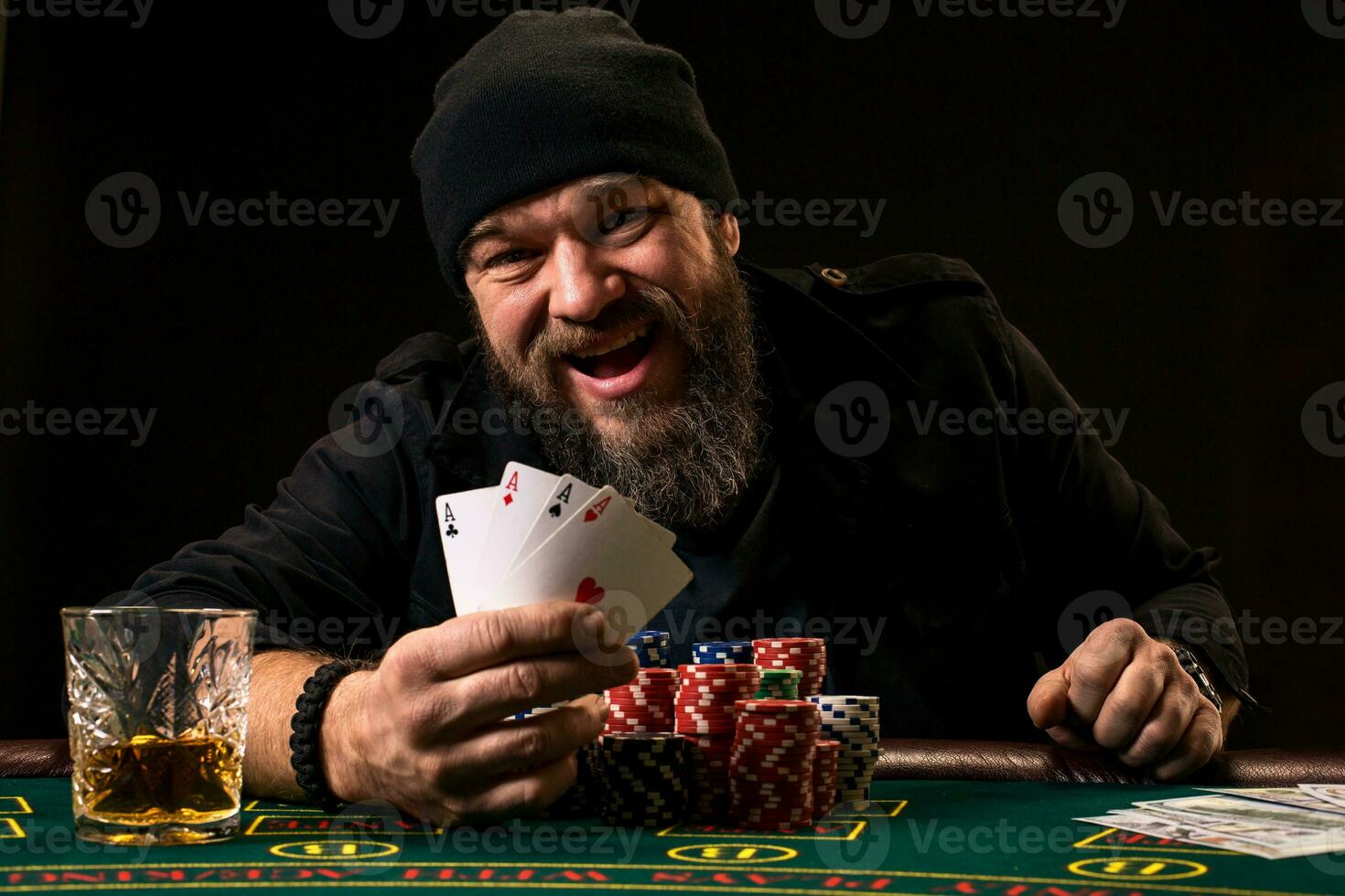 Bearded man with cigar and glass sitting at poker table and screaming isolated on black photo