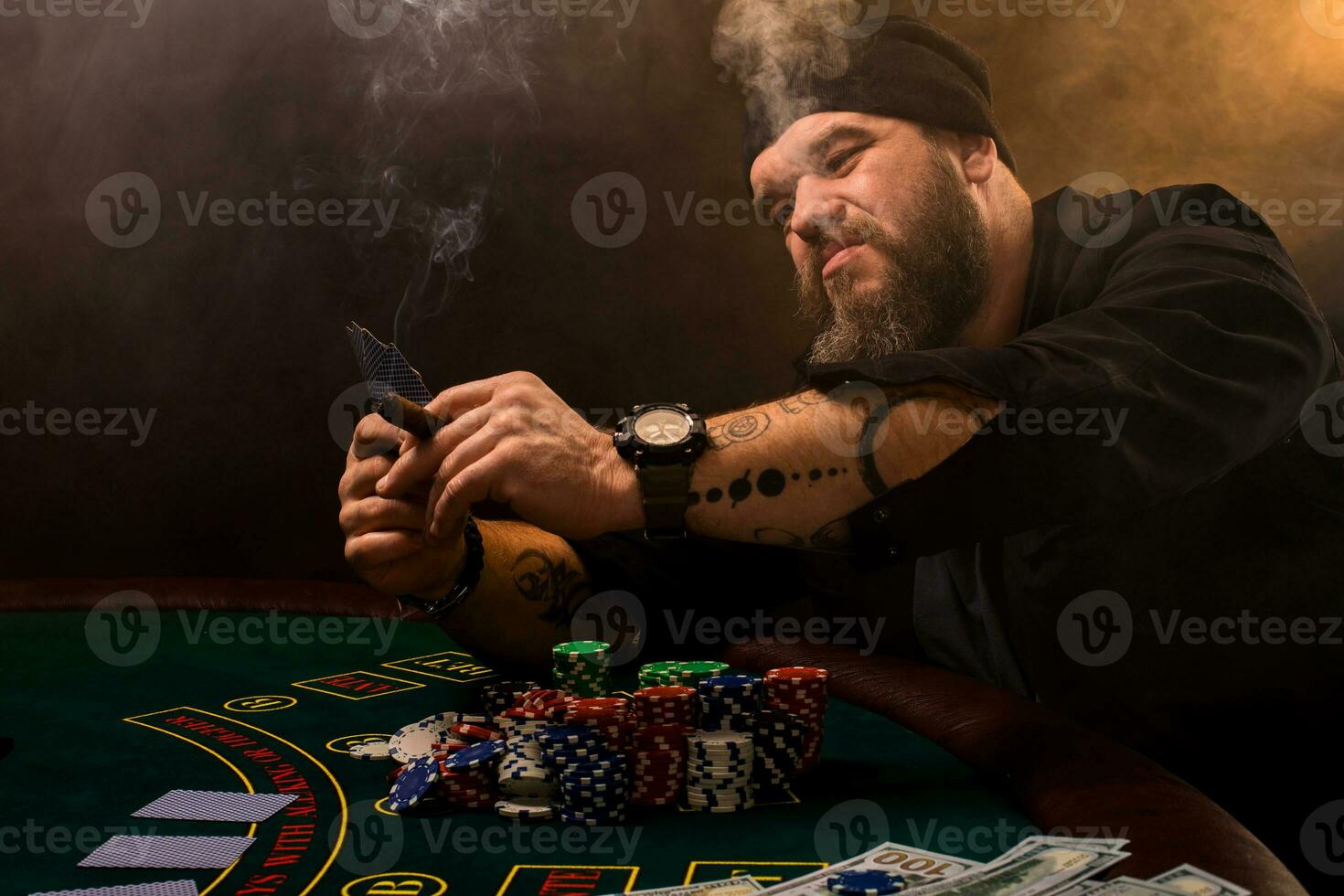 Bearded man with cigar and glass sitting at poker table in a casino. Gambling, playing cards and roulette. photo