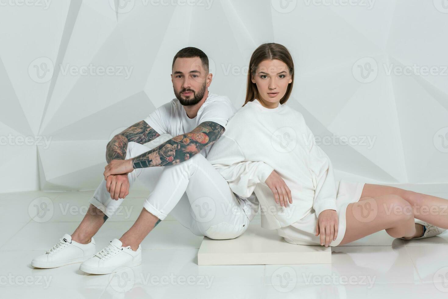 Casual couple near a white wall, man and woman in white clothing. photo