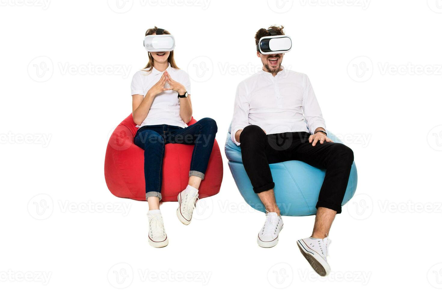 Excited young couple experiencing virtual reality seated on beanbags isolated on white background photo