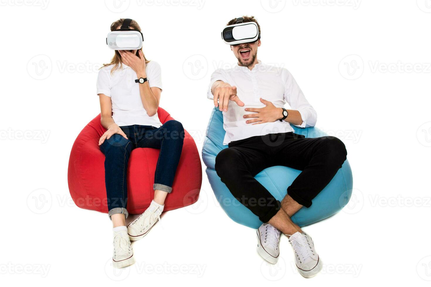 Excited young couple experiencing virtual reality seated on beanbags isolated on white background photo