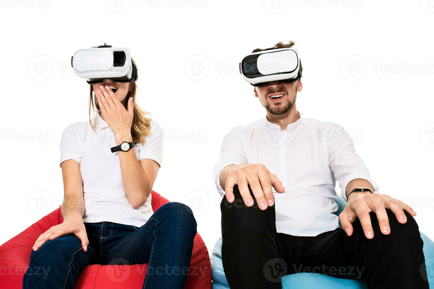 Excited young couple experiencing virtual reality seated on beanbags isolated on white background photo