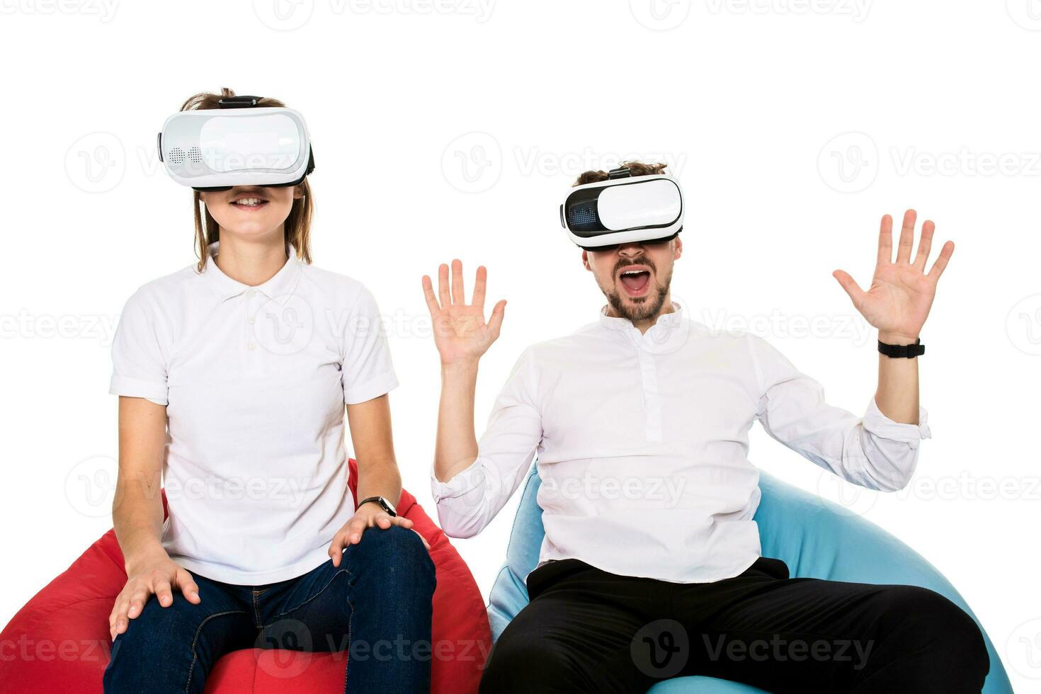 Excited young couple experiencing virtual reality seated on beanbags isolated on white background photo
