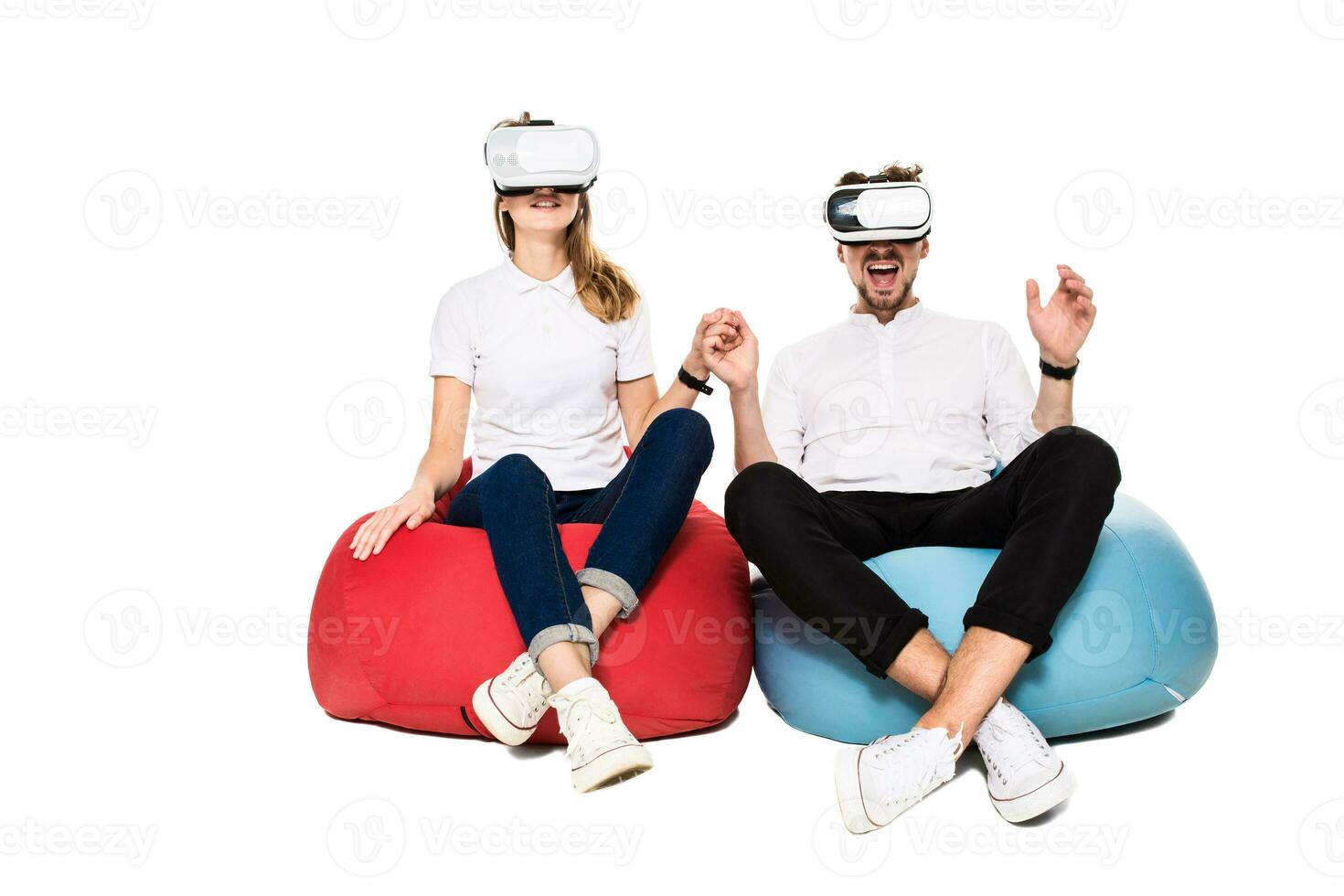 Excited young couple experiencing virtual reality seated on beanbags isolated on white background photo