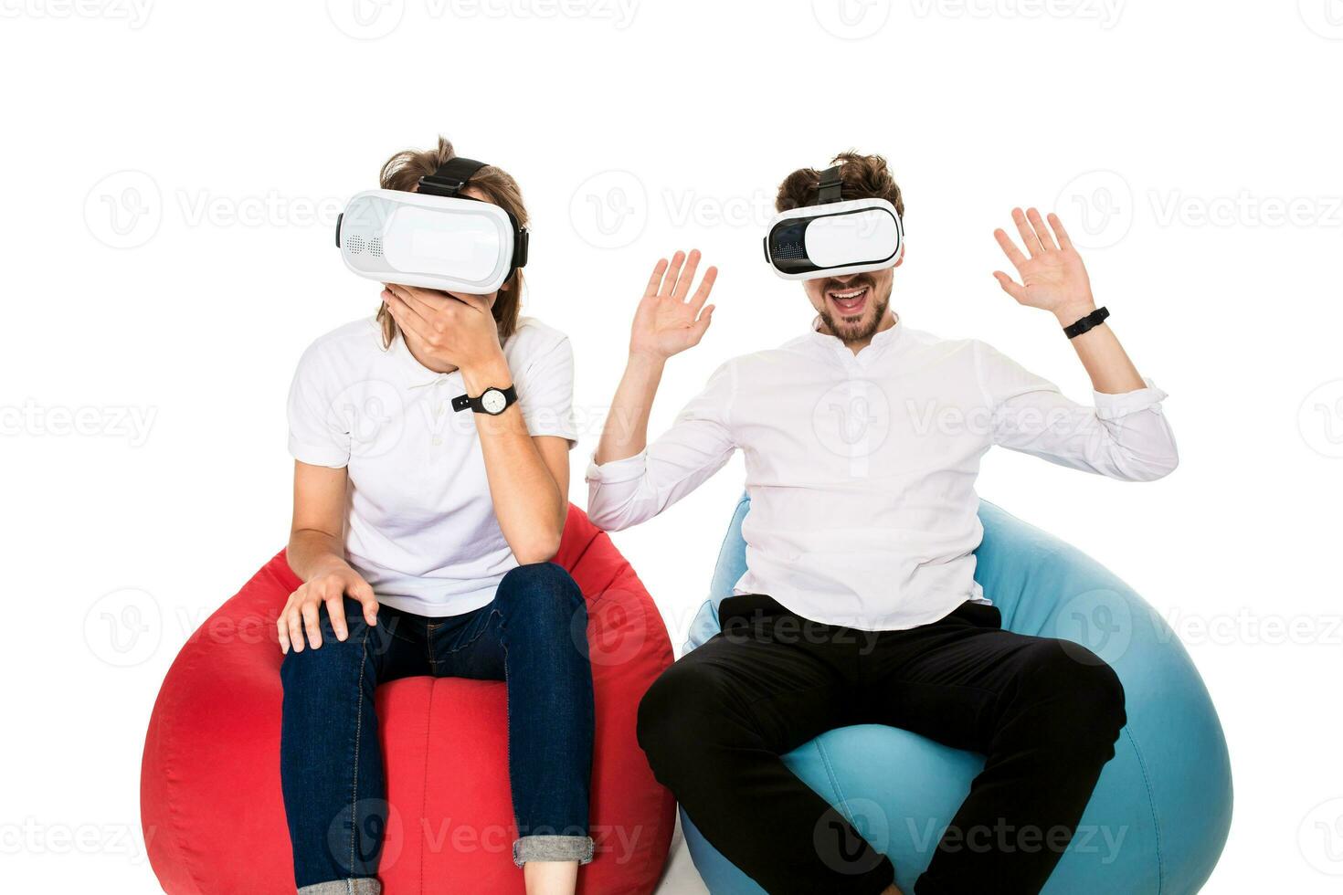 Excited young couple experiencing virtual reality seated on beanbags isolated on white background photo