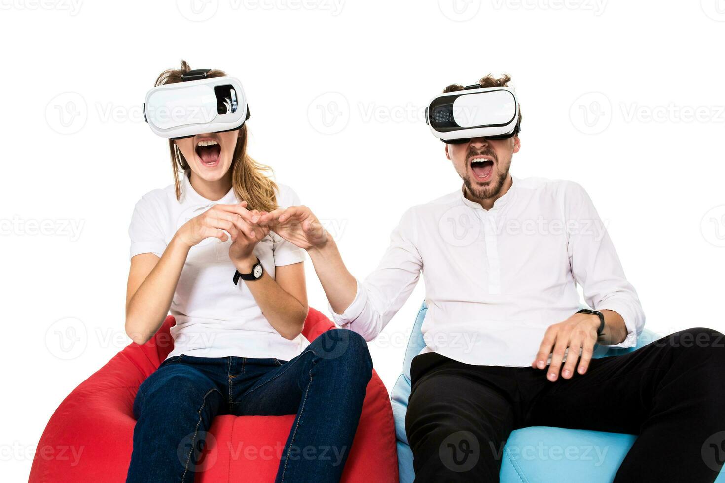 Excited young couple experiencing virtual reality seated on beanbags isolated on white background photo