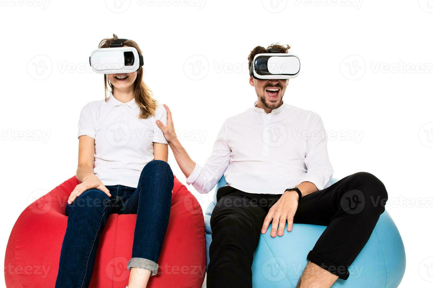 Excited young couple experiencing virtual reality seated on beanbags isolated on white background photo