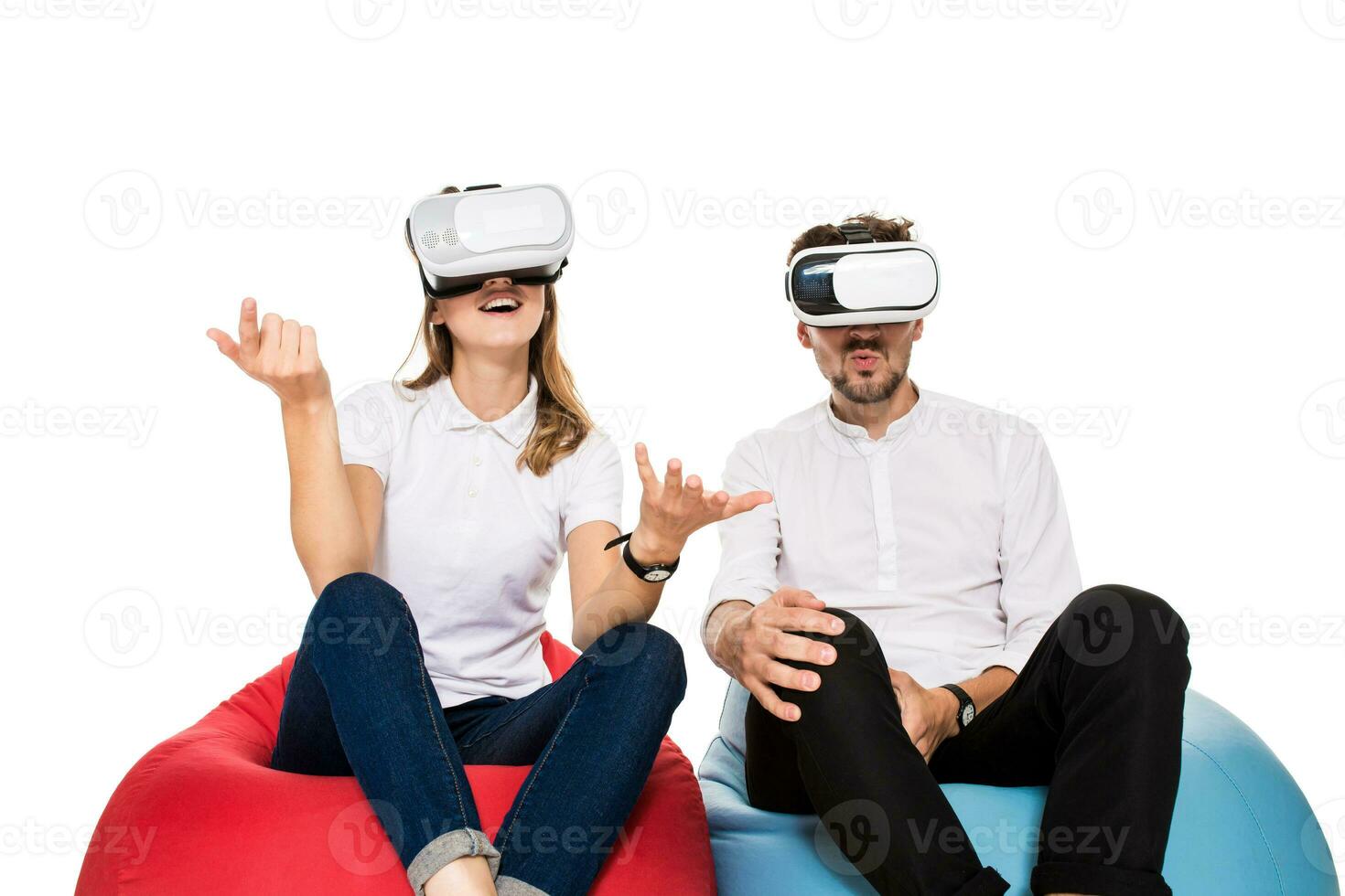 Excited young couple experiencing virtual reality seated on beanbags isolated on white background photo