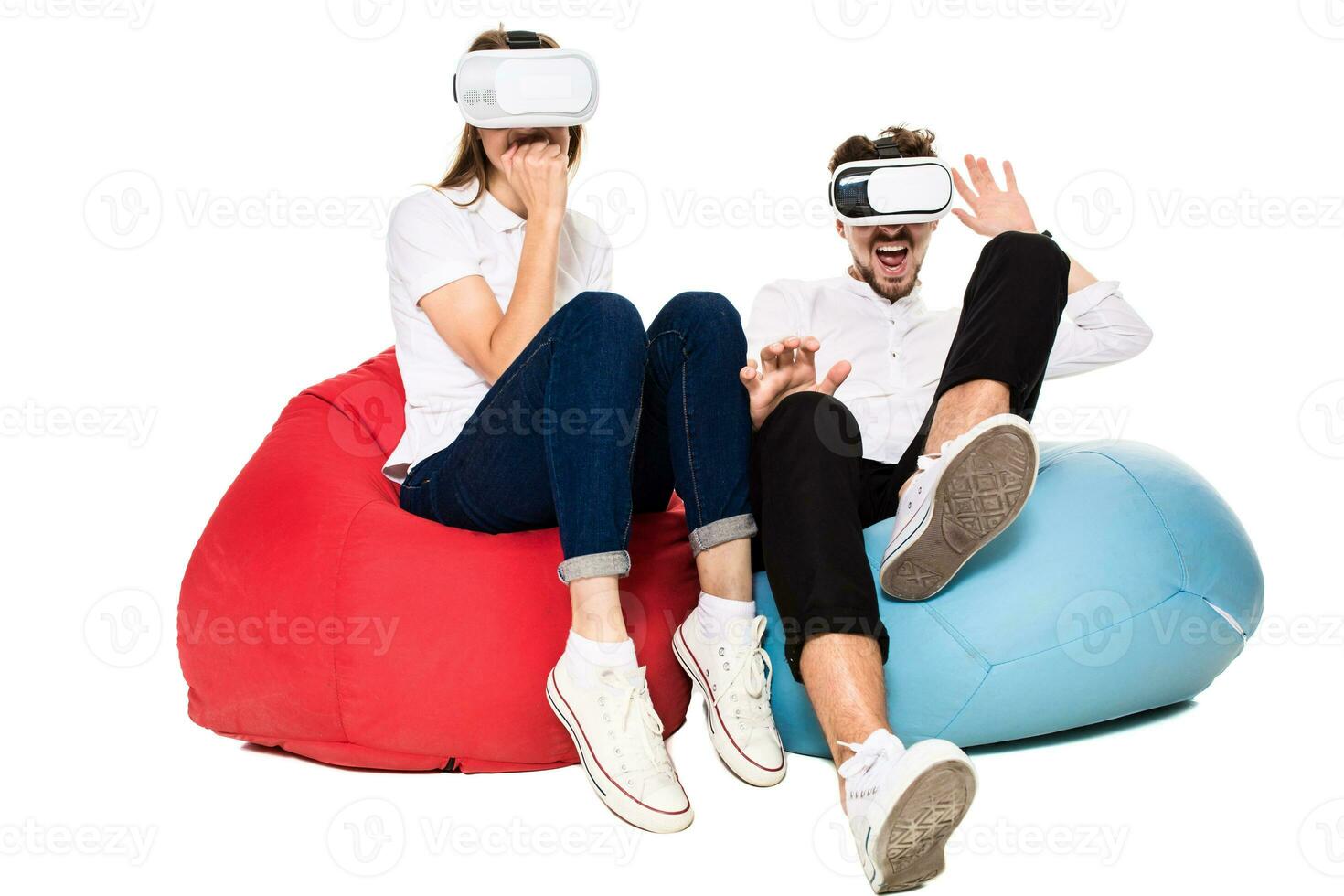 Excited young couple experiencing virtual reality seated on beanbags isolated on white background photo