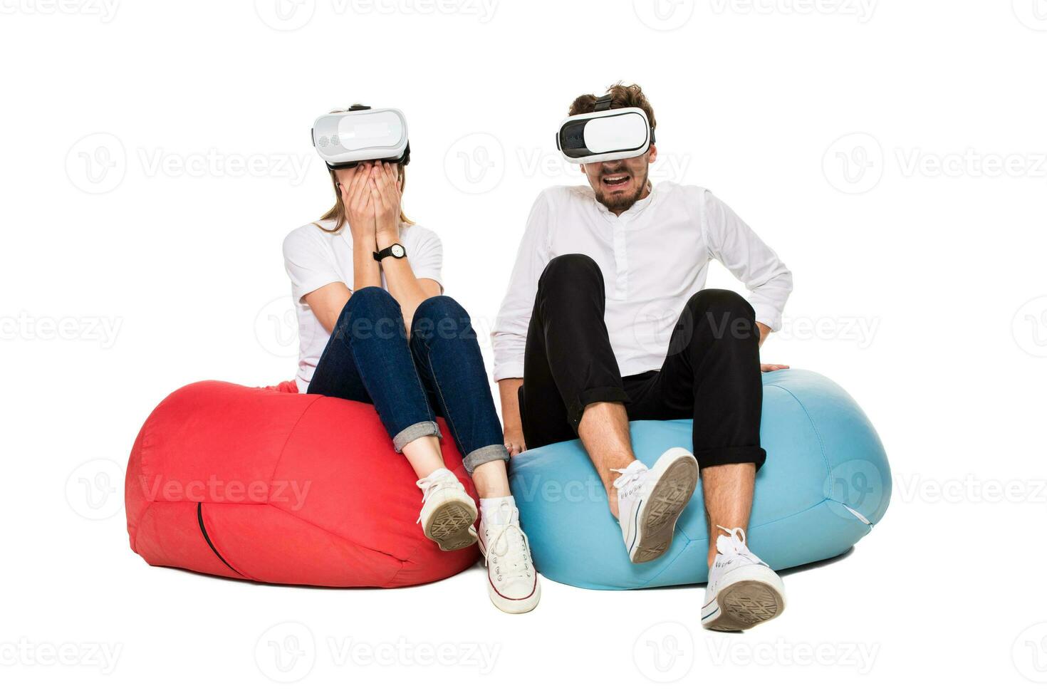 Excited young couple experiencing virtual reality seated on beanbags isolated on white background photo