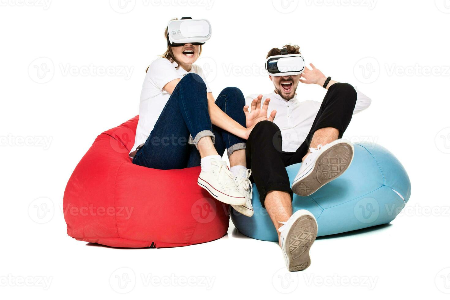 Excited young couple experiencing virtual reality seated on beanbags isolated on white background photo