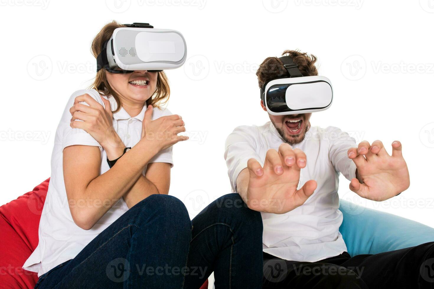 emocionado joven Pareja experimentando virtual realidad sentado en bolsas de frijol aislado en blanco antecedentes foto