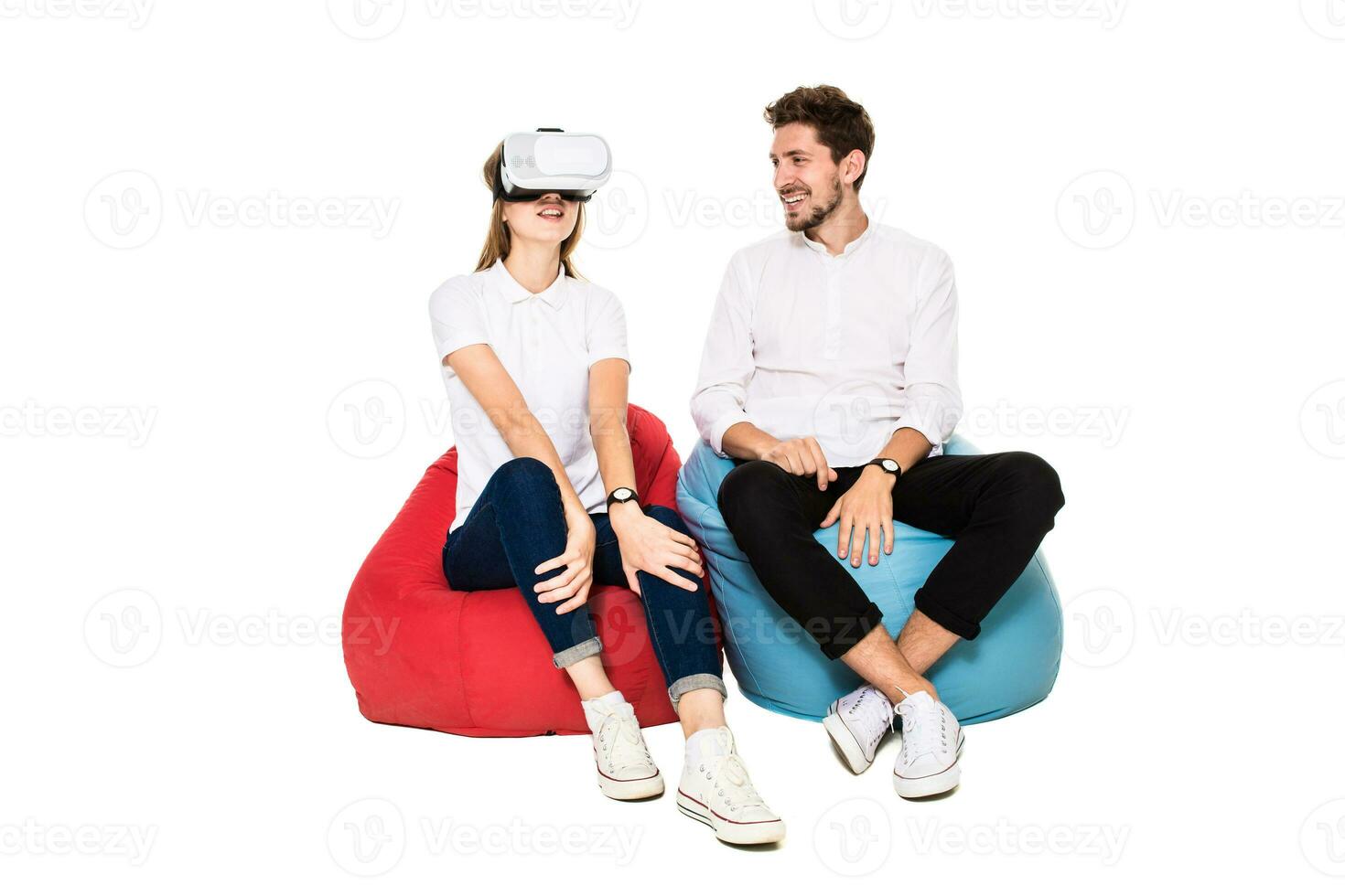 Smiling friends experiencing virtual reality glasses seated on beanbags isolated on white background. photo