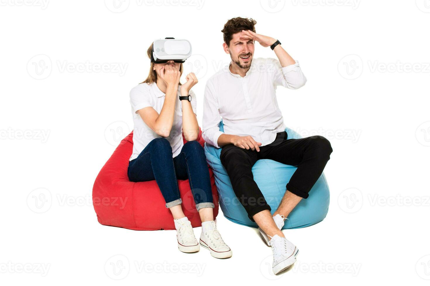 Smiling friends experiencing virtual reality glasses seated on beanbags isolated on white background. photo