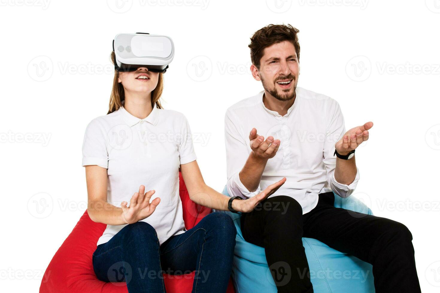 Excited young couple experiencing virtual reality seated on beanbags isolated on white background photo