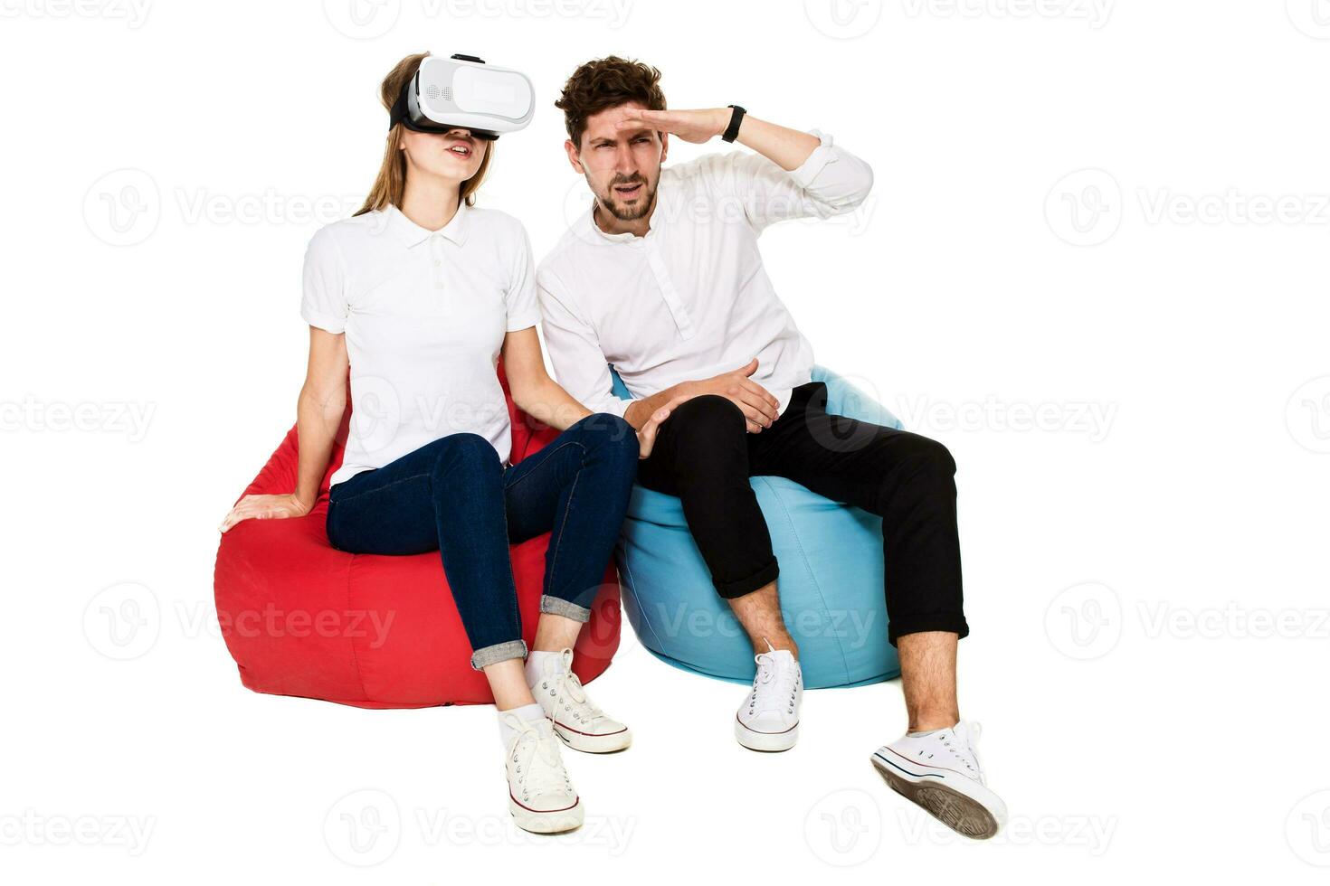 Excited young couple experiencing virtual reality seated on beanbags isolated on white background photo