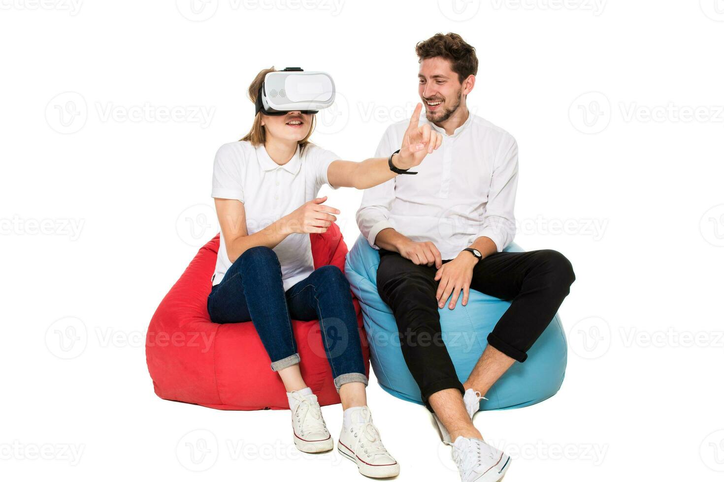 Smiling friends experiencing virtual reality glasses seated on beanbags isolated on white background. photo