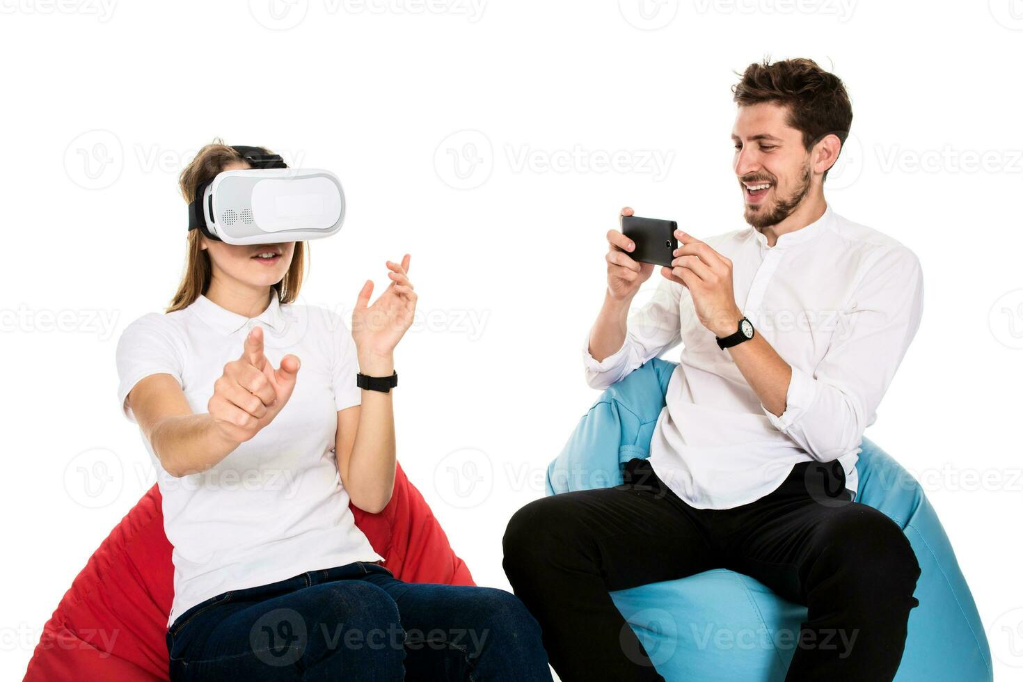 Smiling friends experiencing virtual reality glasses seated on beanbags isolated on white background. photo
