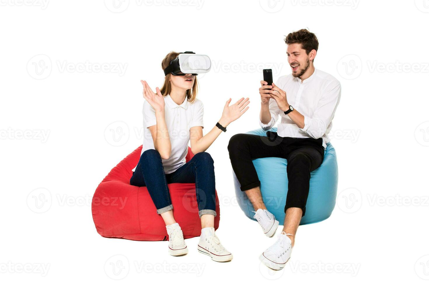 Smiling friends experiencing virtual reality glasses seated on beanbags isolated on white background. photo