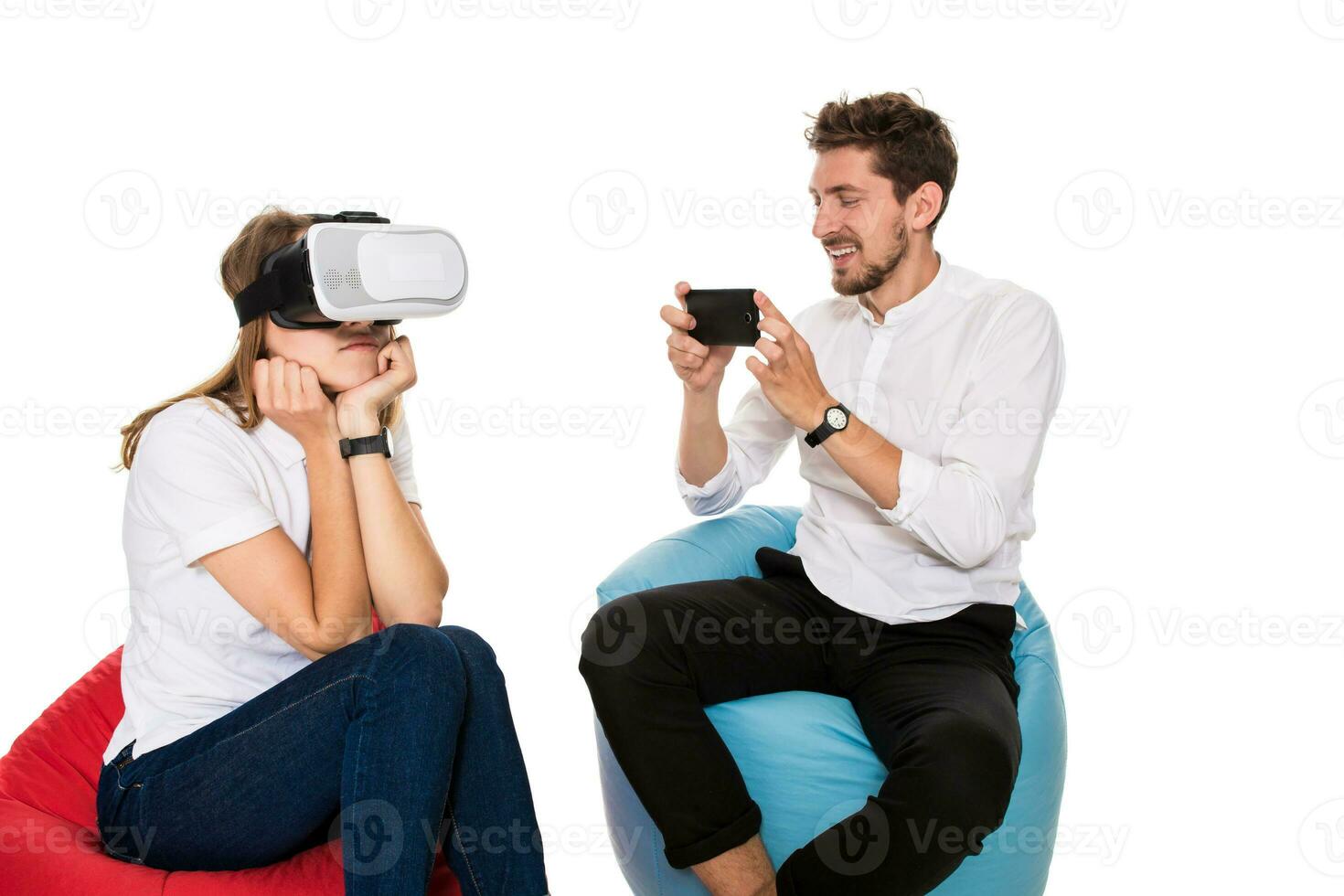 Excited young couple experiencing virtual reality seated on beanbags isolated on white background photo