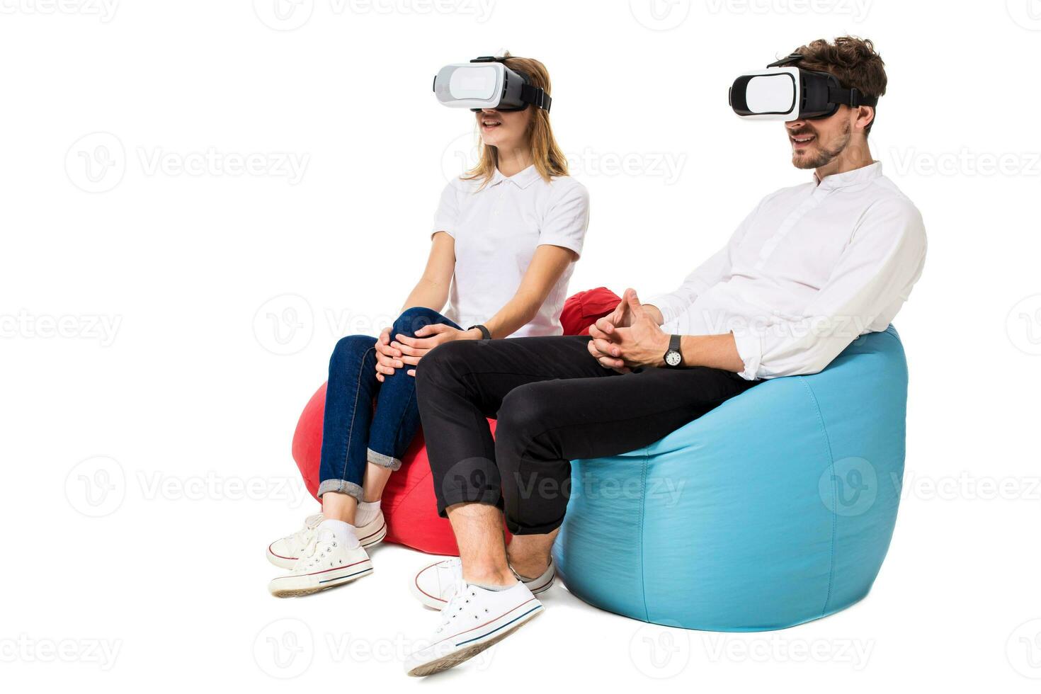 Excited young couple experiencing virtual reality seated on beanbags isolated on white background photo