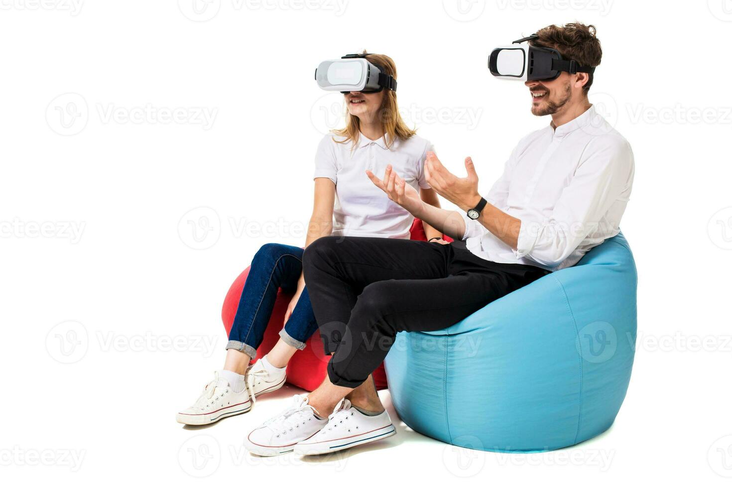 Excited young couple experiencing virtual reality seated on beanbags isolated on white background photo