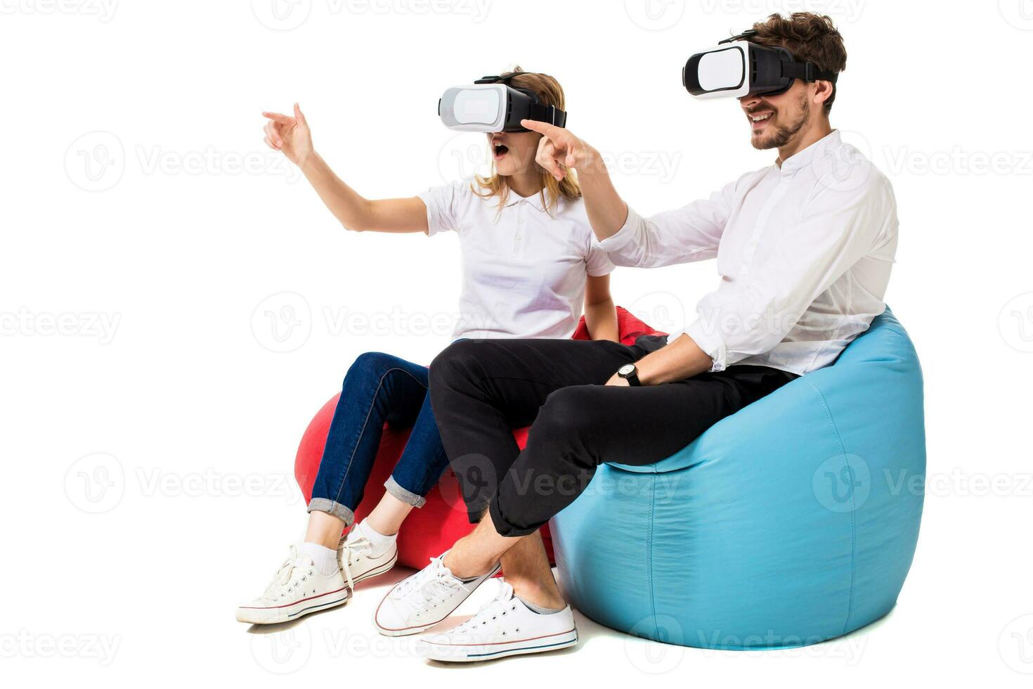 Excited young couple experiencing virtual reality seated on beanbags isolated on white background photo