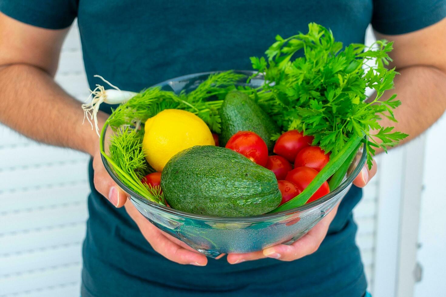 A man holds a large bowl with fresh vegetables and herbs. photo