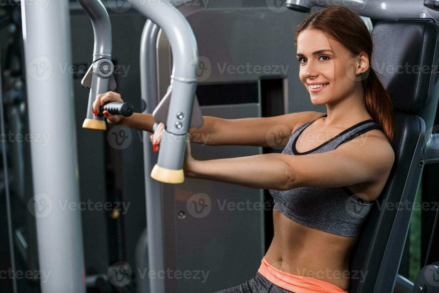 Muscular young woman doing exercises on the simulator in the gym photo