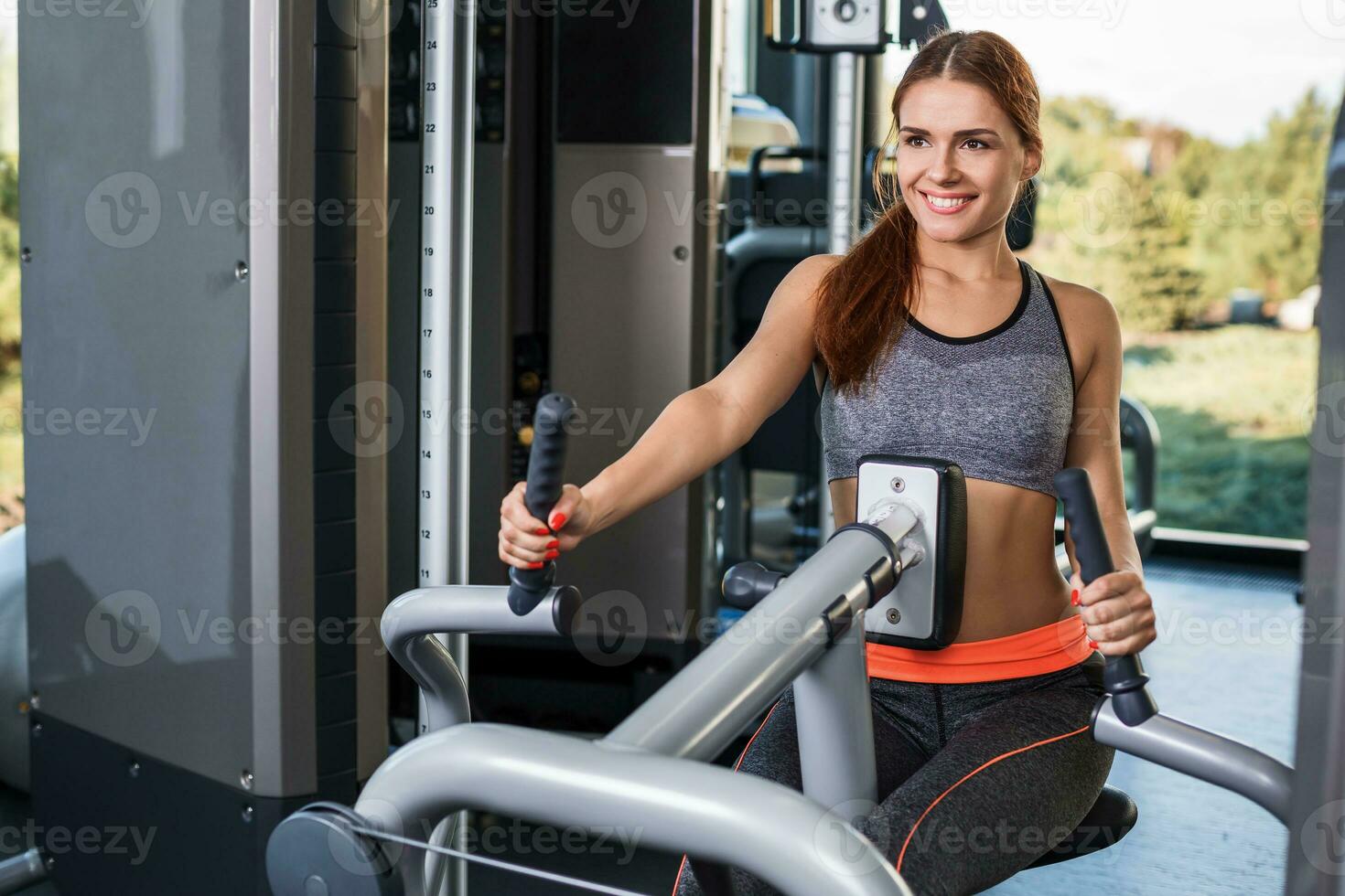 Muscular young woman doing exercises on the simulator in the gym photo