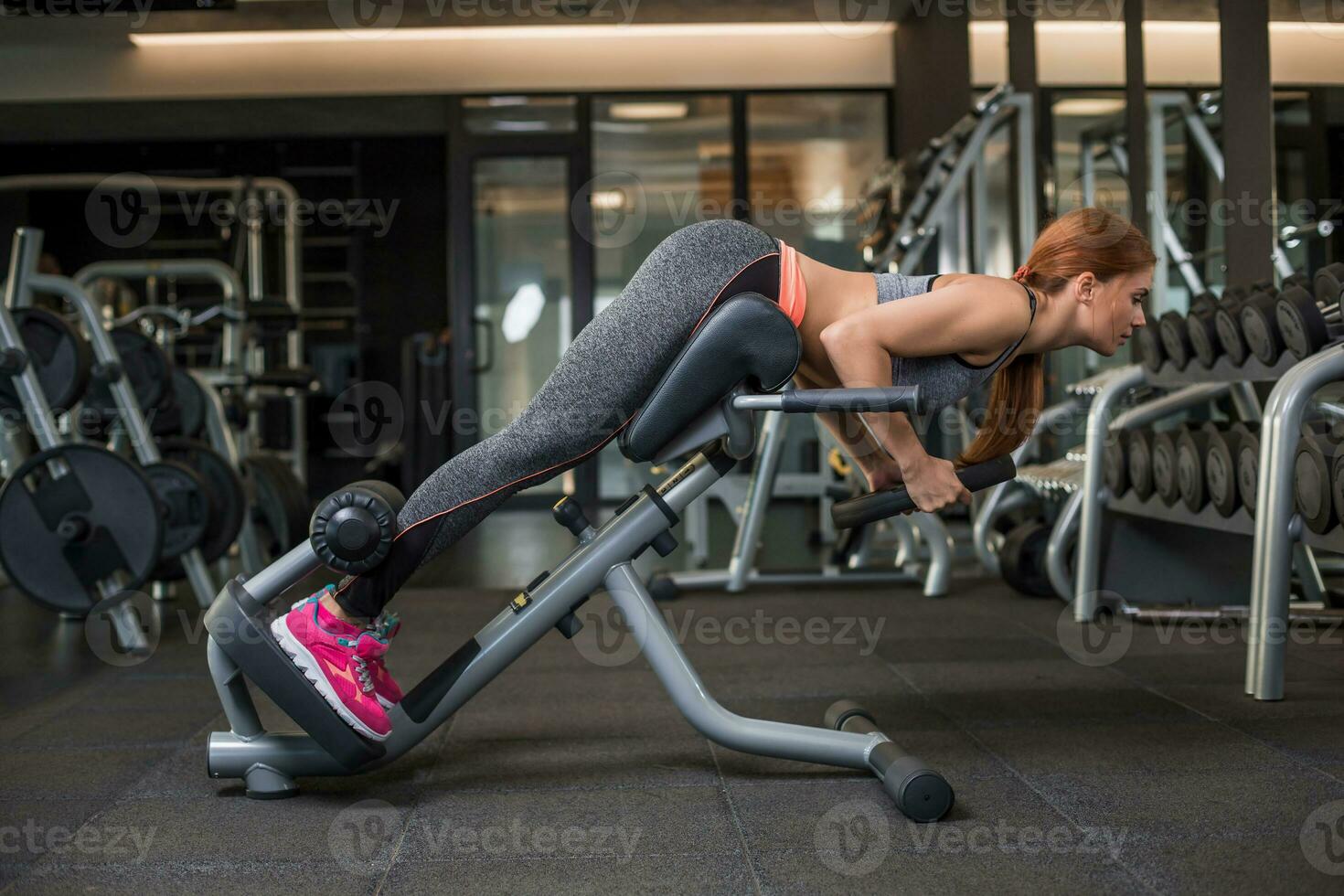 Muscular young woman doing exercises on the simulator in the gym photo