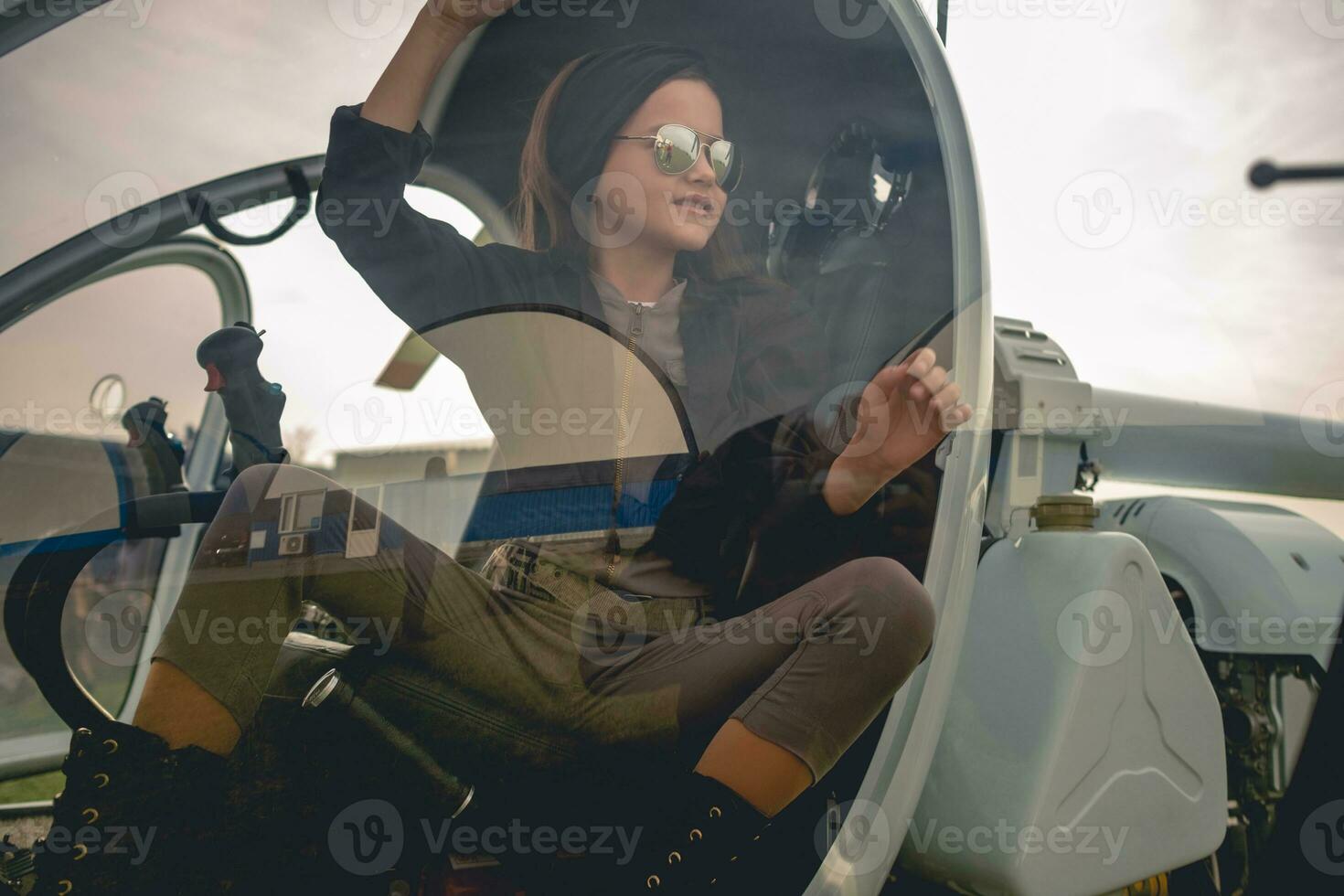 View through glass of helicopter cockpit of smiling preteen girl on pilots seat photo