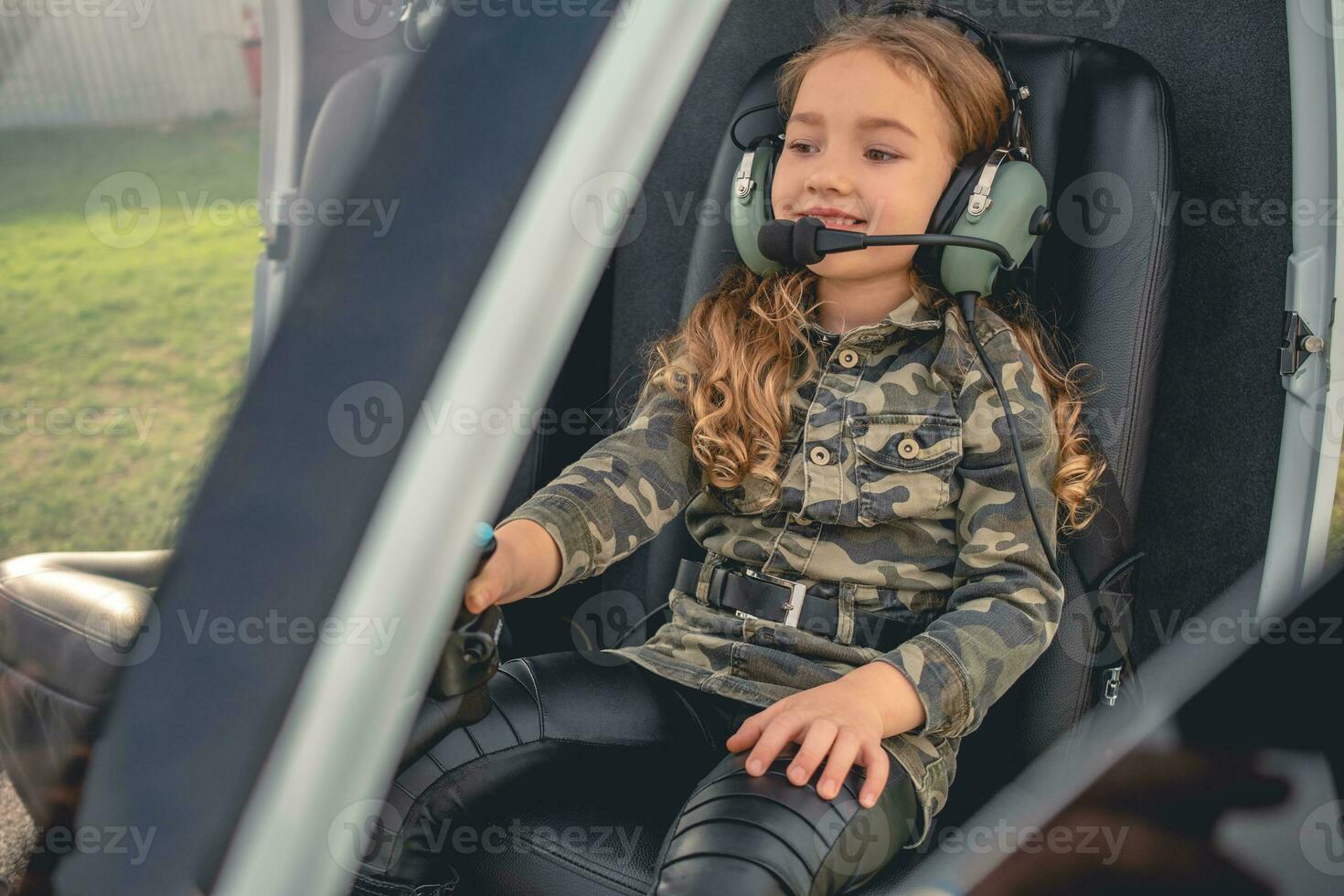 Cheerful tween girl in headset sitting on pilot seat in helicopter photo