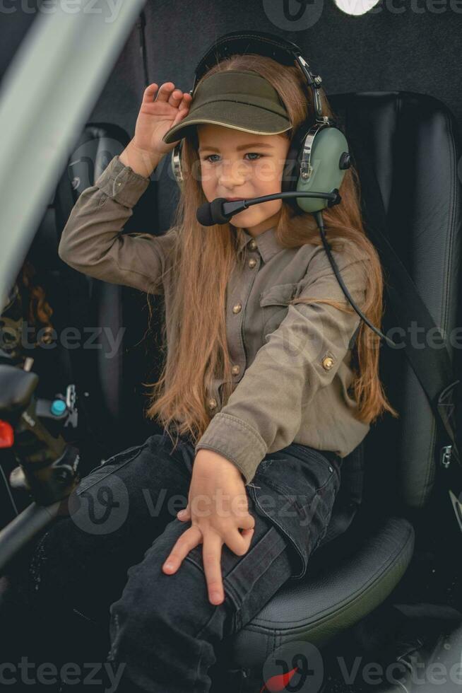 Interested preteen girl in headset sitting on pilot seat in helicopter photo