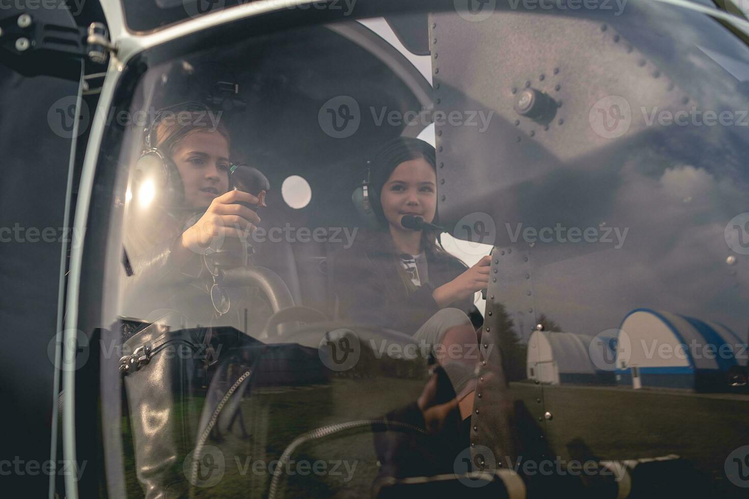 Tween girls in headsets sitting on pilot seats in helicopter photo