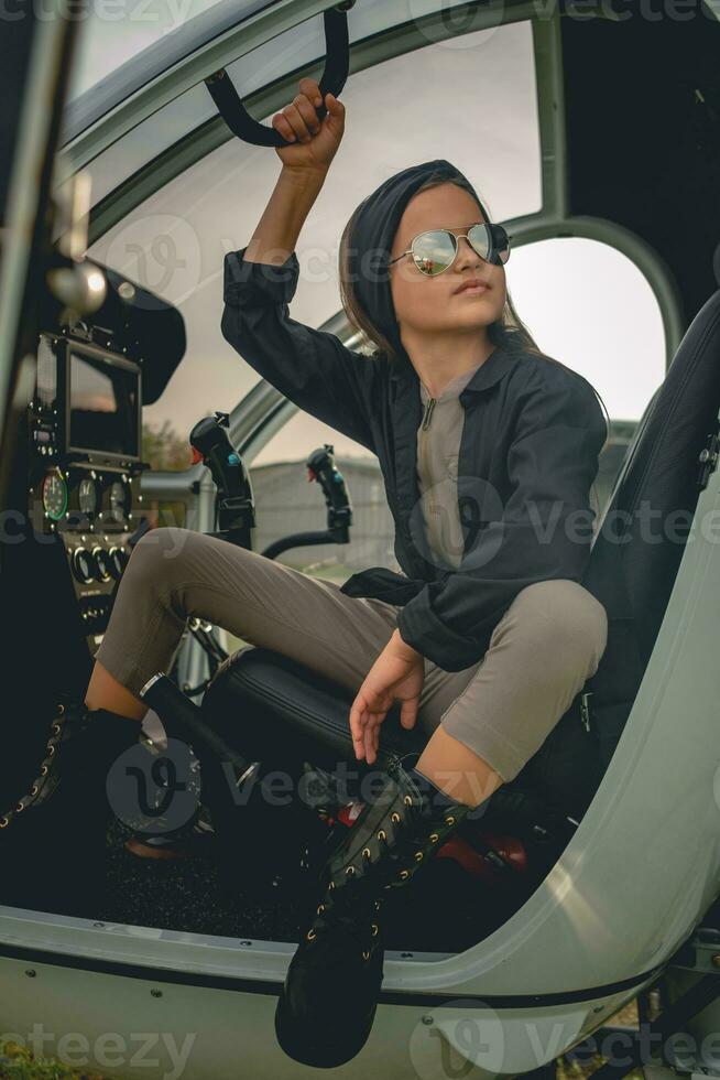 Tween girl in mirrored sunglasses sitting on pilots seat in open helicopter photo
