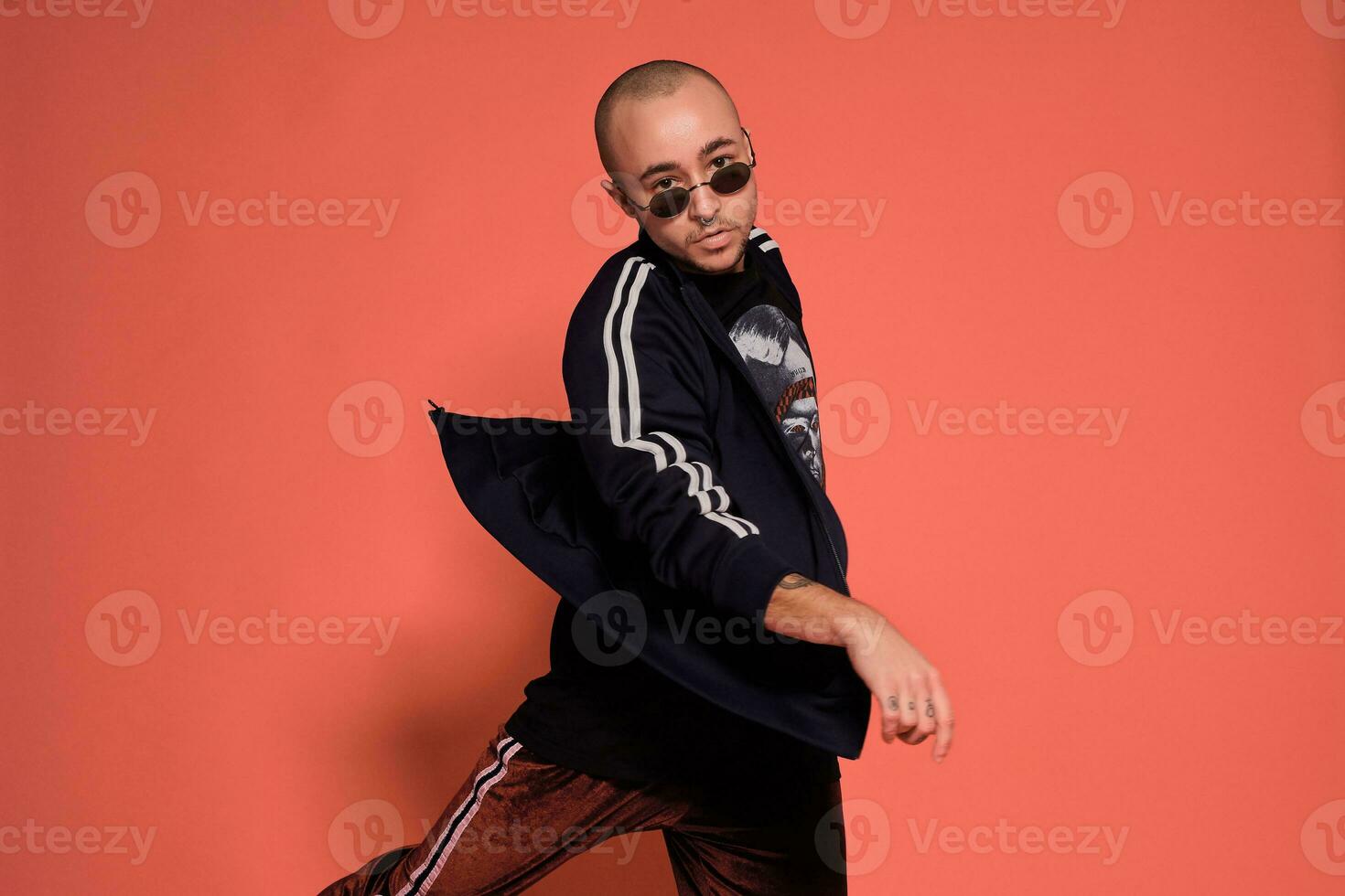 Studio shot of a young tattoed bald man posing against a pink background. 90s style. photo